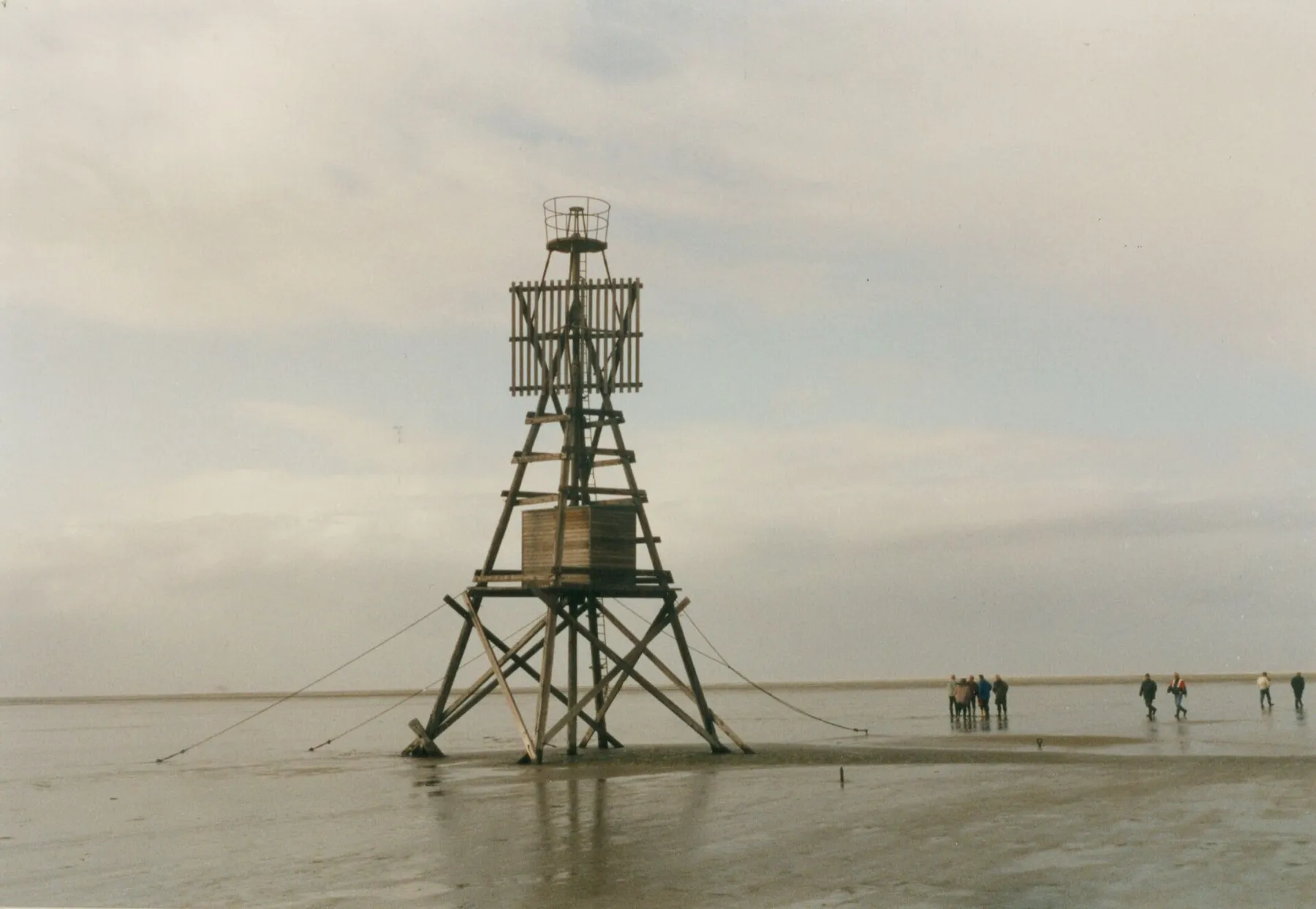 Houten baken op de Engelmansplaat in de Waddenzee, op het natte wad, met wandelaars in de verte